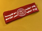 Red polyester tie-back headband featuring the emblem and Arabic script of the National Resistance Brigades, Martyr Omar Al-Qassem Forces, affiliated with the Democratic Front for the Liberation of Palestine (DFLP).