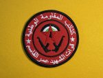 Red circular patch with a black border, featuring a red star and crossed black rifles in the center, surrounded by Arabic script. The patch represents the National Resistance Brigades, Martyr Omar Al-Qassem Forces, the armed wing of the Democratic Front for the Liberation of Palestine (DFLP).