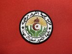 This patch features the emblem of the National Liberation Front (FLN) of Algeria, with intricate Arabic text, a flame, star, crescent, and a sunburst design. Measuring 3.5 inches in diameter, this patch is available with Velcro backing, iron-on backing, or no backing for sewing, making it a versatile addition to any collection. Ideal for collectors, reenactors, and historians.