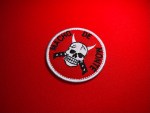 Embroidered circular Macho de Monte patch with a red background, white satin border, horned skull at center, crossed blades beneath the skull, and black “Macho de Monte” text around the edge.