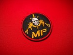 Round embroidered MF faction patch with skull, crossed rifles, and dagger in gold and white on a black background with red satin border.