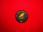 Round black and gold embroidered MF MZ “100% Mayiza” patch with horse head emblem, photographed on a red background.