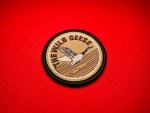 Round 2.5-inch embroidered “The Wild Geese” beret patch in subdued tan and brown, featuring a flying goose over water with black satin border.