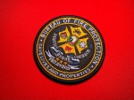 Circular embroidered Bureau of Fire Protection Philippines emblem patch with a gold Malta cross, firefighting symbols, and the motto “Save Lives and Properties” on a black background, displayed on red fabric.
