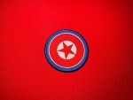 North Korean Ministry of Social Security embroidered DPRK roundel shoulder patch with red star, white center, red field and blue border on a red background.