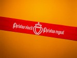 Red SSPX tie-back headband featuring the white Latin text “Christus vincit, Christus regnat” and the crowned intertwined Sacred Heart of Jesus and Heart of Mary emblem.