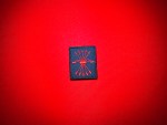 Spanish Falange replica patch with a red yoke and five arrows embroidered on dark blue cloth, displayed on red fabric.