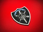 Angled close-up of the El Salvador Comando Especial Antiterrorista (CEAT) replica patch, showing detailed white embroidery, a black shield and white border on red fabric.